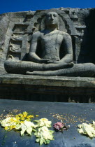 Sri Lanka, polonnaruwa, Gal Vihara, lotus flower offerings left in front of giant seated Buddha figure carved into cliff.