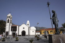 Spain, Canary Islands, Tenerife, Santiago del Teide, Exterior of church with statue of Guanche chief in the foreground.