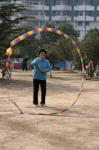 China, Jiangsu, Nanjing, Woman in a blue sweater and sneekers relaxing in a municipal park spinning a top with a multicoloured tail with an apartment block in the background.