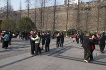 China, Jiangsu, Nanjing, Retired couples enjoying ballroom dancing beneath the old Ming city wall in Xuanwu Lake park with a modern skyscraper in the background.