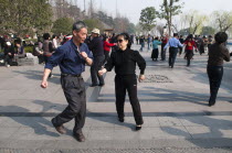 China, Jiangsu, Nanjing, Retired couples dancing beneath the Ming city wall at Xuanwu Lake Park, Couple in foreground swinging arms in modern dance.