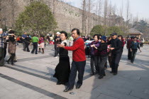 China, Jiangsu, Nanjing, Retired couples dancing beneath the Ming city wall at Xuanwu Lake Park, Couples in foreground dancing the tango in a line.
