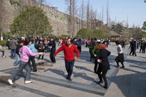 China, Jiangsu, Nanjing, Retired couples dancing beneath the Ming city wall at Xuanwu Lake Park, Man in red sweater with arm extended to woman in pink sweater.