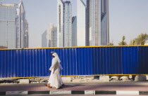 United Arab Emirates, Dubai, Arab men dressed in traditional Dishdasha walking past construction site with Sheikh Zayed Road behind.