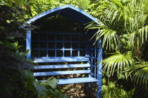 Blue coloured bench seat in urban garden with palms.