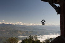 Nepal, Nagarkot, View across clouded valley towards Himalayan mountains, wind chime hanging from traditionally carved corner of building in foreground.