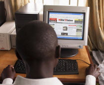 Uganda, Kabarole District, Fort Portal Teacher Training College Student teacher sat at a PC reading a National Newspaper