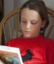 Education, 9-year old girl in vivid red t-shirt sat reading book.