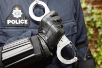 Detail of Police officer wearing body armour and holding Hand Cuffs.