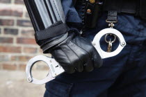 Detail of Police officer wearing body armour and holding Hand Cuffs.