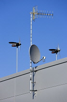 Direct-drive wind generators designed for electric microgeneration applications attached to industrial unit beside satellite dish and analogue television aerial.