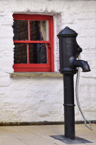 Ireland, Derry, Derry Craft Village, Old water pump with small red window in background.