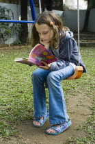 Education, Reading, 10 year old girl reading on swing in garden.