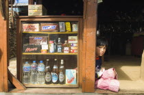 Nepal, Pokhara. Girl sat in a  shop doorway on a trekking route with western snacks for sale.