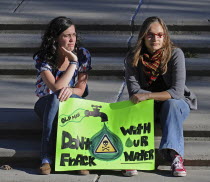 Canada, Alberta, Lethbridge, Two local women atsitting on stone steps at an anti-fracking demonstration holding a green protest sign. Oldman River, which runs through Lethbridge, is the source of the...