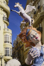 Spain, Valencia Province, Valencia, Female Papier Mache figure with a horse on her head  in the street during Las Fallas festival.
