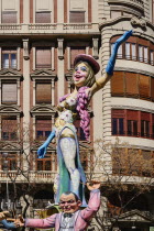 Spain, Valencia Province, Valencia, Papier Mache figure of a woman standing on another figures shoulders  in the street during Las Fallas festival.