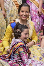 Spain, Valencia Province, Valencia, Reina Fallera in traditional Valencian costume taking a break with young child also in traditional Valencian costume during Las Fallas festival.