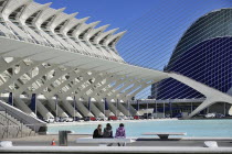 Spain, Valencia Province, Valencia, La Ciudad de las Artes y las Ciencias, City of Arts and Sciences, Principe Felipe Science Museum, General view of the building with girls on seat in the forground a...