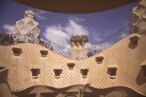 Spain, Catalonia, Barcelona, La Pedrera or Casa Mila on Passeig de Gracia, designed by Antoni Gaudi, view of the roof through mesh covered attic window.