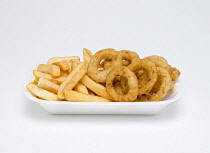 Food, Cooked, Vegatables, deep fried onion rings in batter and potato chips in an insulated polystyrene foam tray on a white background.