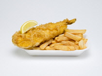 Food, Cooked, Fish, A portion of battered deep fried cod with a slice of lemon and potato chips in an insulated polystyrene foam tray on a white background.