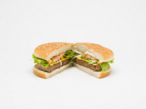 Food, Cooked, Meat, Single cheesburger with salad and tomato ketchup in a bun cut in half and open on a white background.