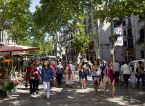 Spain, Catalonia, Barcelona, People walking along the central tree shaded walkway of La Rambla historic avenue past flower stalls in the Old Town district.