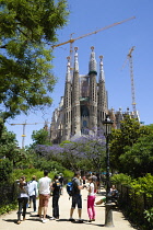 Spain, Catalonia, Barcelona, Tourists in a small park viewing the basilica church of Sagrada Familia deisigned by Antoni Gaudi in the Eixample district.