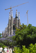 Spain, Catalonia, Barcelona, Tourists in a park viewing the basilica church of Sagrada Familia deisigned by Antoni Gaudi in the Eixample district.