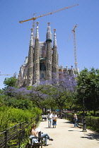 Spain, Catalonia, Barcelona, Tourists in a small park viewing the basilica church of Sagrada Familia deisigned by Antoni Gaudi in the Eixample district.