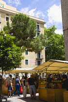 Spain, Catalonia, Barcelona, People among shaded market stalls in a small tree lined square in the Gothic Quarter.