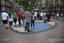 Spain, Catalonia, Barcelona, Tourist walking along the tree lined avenue of La Rambla with Joan Miro mosaic in the pavement.