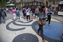 Spain, Catalonia, Barcelona, Tourist walking along the tree lined avenue of La Rambla with Joan Miro mosaic in the pavement.