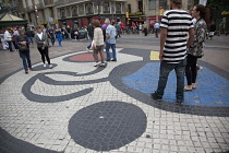 Spain, Catalonia, Barcelona, Tourist walking along the tree lined avenue of La Rambla with Joan Miro mosaic in the pavement.