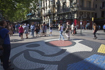 Spain, Catalonia, Barcelona, Tourist walking along the tree lined avenue of La Rambla with Joan Miro mosaic in the pavement.