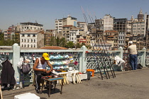 Turkey, Istanbul, Man fishing and man selling fishing tackle on Galata Bridge.