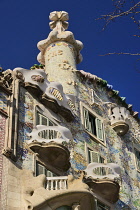 Spain, Catalunya, Barcelona, Casa Batllo by Antoni Gaudi, angular view of the upper section of the exterior facade showing window balconies and cross on roof.