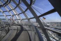 Germany, Berlin, Reichstag Parliament Building, Interior view of the Glass Dome designed by Norman Foster with couple walking around the ramp and German flag visible outside.