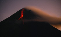 Indonesia, Java, Mount Merapi, Volcano erupting at dawn with lava flowing in a stream down one side.