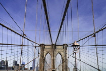 USA, New York, Brooklyn Bridge. View across bridge towards Manhattan skyline part framed by central stone tower and intersected by steel wires and suspension cables.