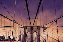 USA, New York, Brooklyn Bridge. View across bridge towards Manhattan skyline part framed by central stone tower and intersected by steel wires and suspension cables.