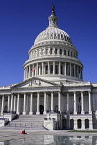 USA, Washington DC, Capitol Building, Angular view of the central section with the dome and American flag at half mast and lady dressed in red sitting out front.