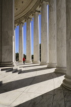 USA, Washington DC, National Mall, Thomas Jefferson Memorial, A tourist strolls among the Ionic columns with long shadows cast by evening sun.