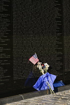 USA, Washington DC, National Mall, Vietnam Veterans Memorial, A section of The Memorial Wall with the names of those killed or missing in action during the Vietnam War, Bunch of flowers and American f...