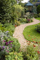 English cottage garden, winding shingle path leading to a gazebo between grass lawn and flowerbed of mixed plant varieties.