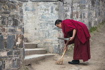 China, Tibet, A buddhist monk in red robe is cleaning the Labrang Monastery steps.