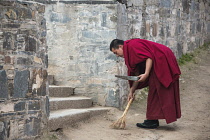 China, Tibet, A buddhist monk in red robe is cleaning the Labrang Monastery steps.