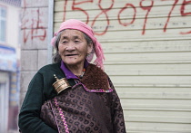 China, Tibet, Gade City, Kind aged Tibetan woman with a small player wheel on a street.