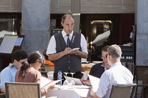 Spain, Madrid, Waiter taking orders from diners at a restaurant in the Plaza Mayor.